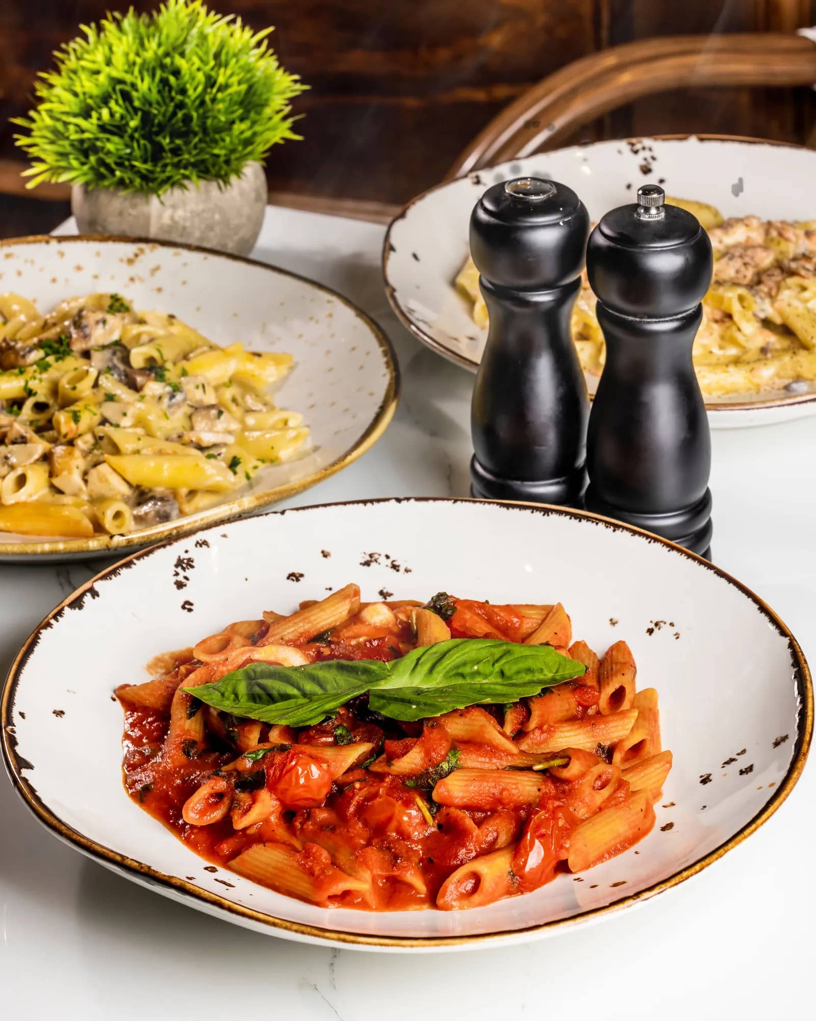 Penne pasta in tomato basil sauce with mushroom pasta dishes and pepper mills on a marble table