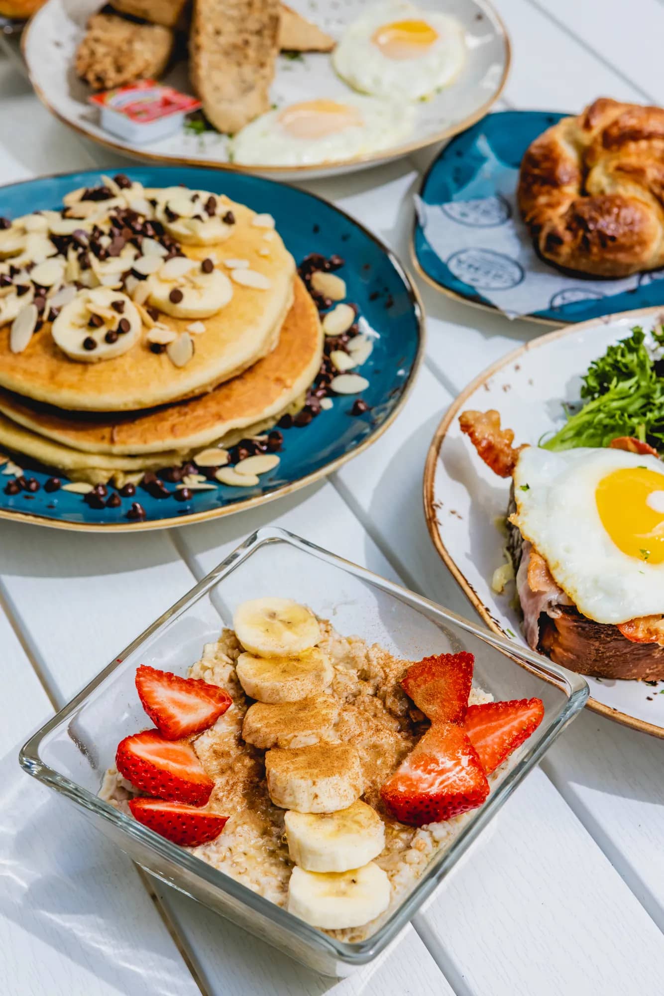 Breakfast spread with chocolate chip banana pancakes, oatmeal bowl, fried eggs and a sandwich