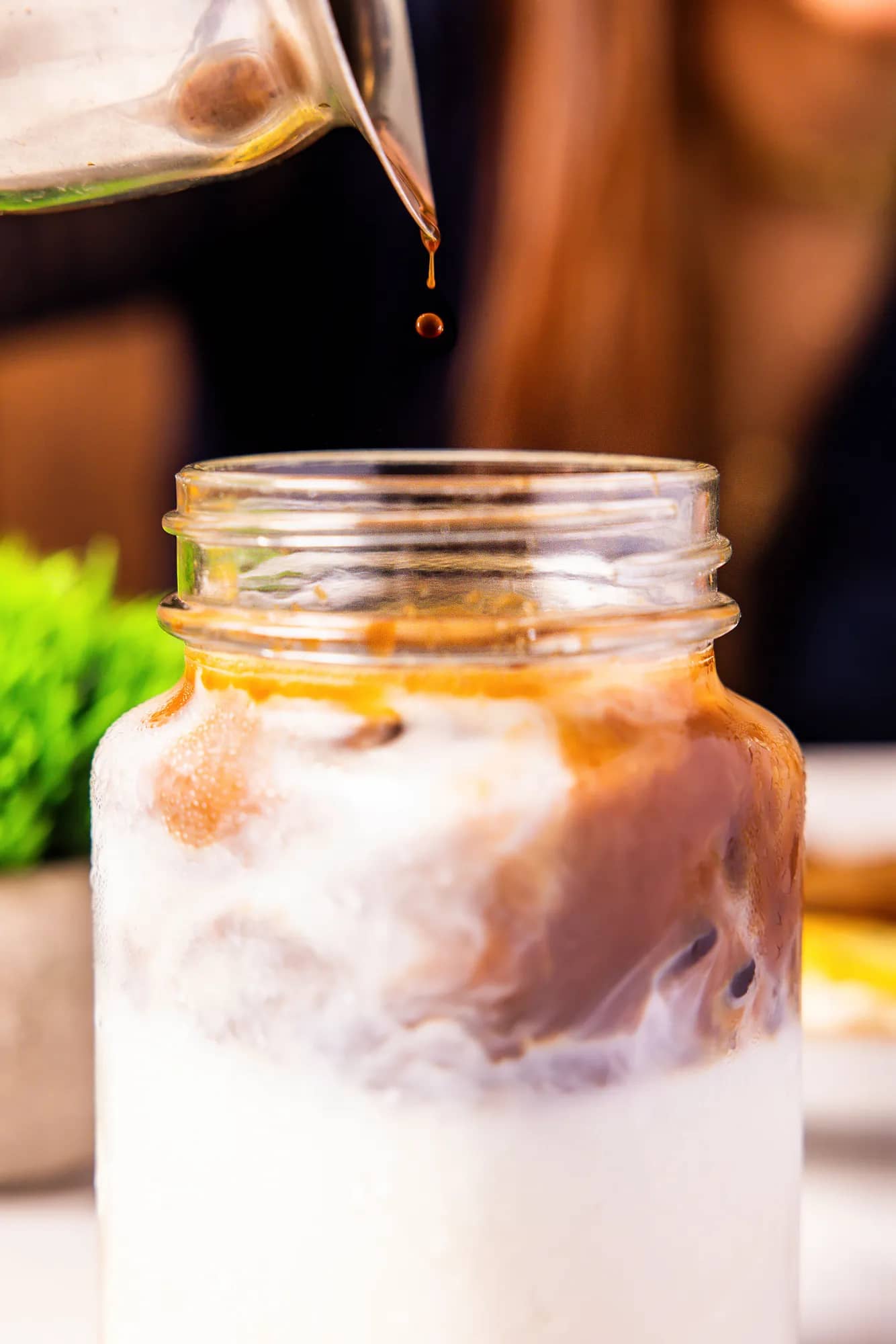 Caramel syrup drizzling into an iced latte in a glass mug